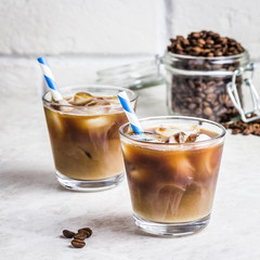 Iced coconut coffee in glass and coffee beans in glass jar on white background. Selective focus, copy space. 