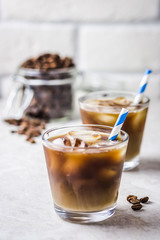 Cinnamon vanilla iced coffee in glass and coffee beans in glass jar on white background. Selective focus, copy space.