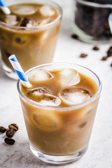 Coconut caramel iced coffee in glass and coffee beans in glass jar on white background. Selective focus, copy space.