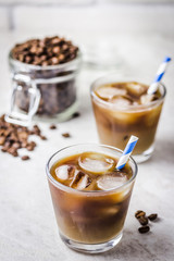 Iced caramel macchiato in glass and coffee beans in glass jar on white background. Selective focus, copy space. 
