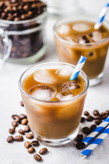 Almond milk iced coffee in glass and coffee beans in glass jar on white background. Selective focus, copy space. 