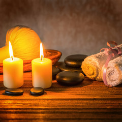 spa composition of white towels, candles with natural light, thai herbal compress ball in basket and zen basalt stones on wooden background, close up