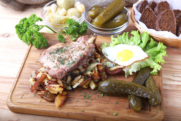 Fried pork with potatoes, egg and pickle cucumber on a wooden board