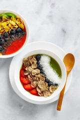 two bowls with different Smoothies from strawberries and kiwi, with Cereals for a healthy Breakfast and berries, chia seeds and coconut chips . Wheat bran and Cornflake. super food