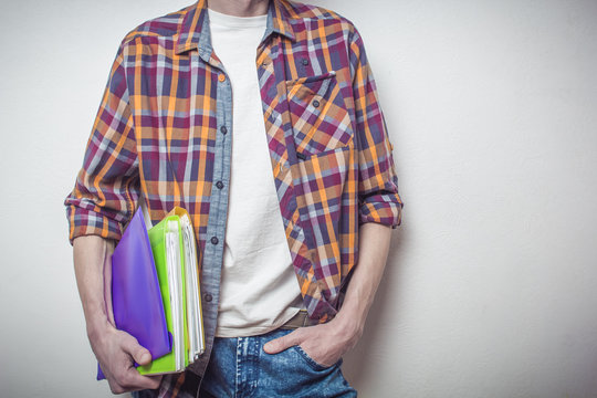 Midsection of a male student in a plaid shirt holding colorful folders and notebooks. University education and learning concept.