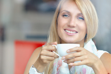 Cheerful woman with cup of coffee sitting in cafe and looking at the window