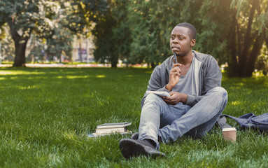 Obraz premium Concentrated african-american studen sitting with notebook on grass