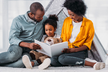 african american parents teaching daughter to read at home