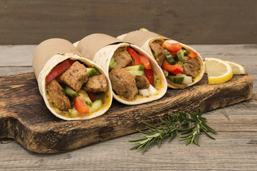 Fresh tortilla wraps with pork meat and fresh vegetables on wooden board. 