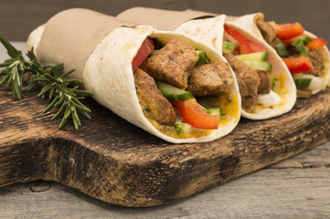 Fresh tortilla wraps with pork meat and fresh vegetables on wooden board. 