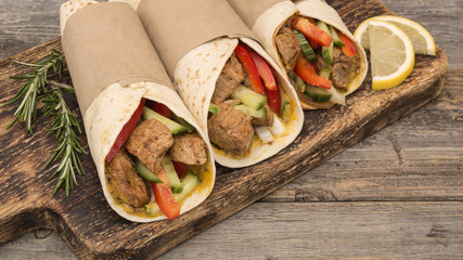 Fresh tortilla wraps with pork meat and fresh vegetables on wooden board. 