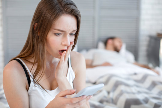 Oh my god. Pretty startled heart-broken woman reading her mans messages while he sleeping and she sitting on the bed