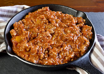 Bolognese sauce in a cooking pan or iron pan. Italian cuisine background with pasta sauce and slate plate.