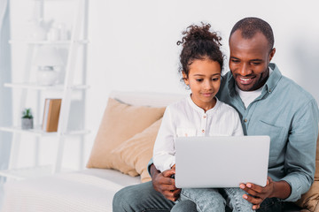 happy african american father and daughter using laptop at home - Powered by Adobe