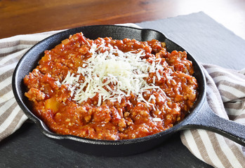 Bolognese sauce with parmesan cheese in a cooking pan or iron pan. Italian cuisine background with pasta sauce and slate plate.