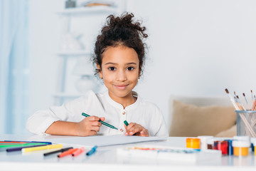 adorable african american kid drawing with felt pens and looking at camera at home