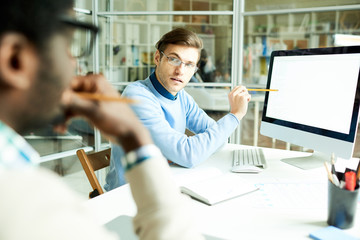 Portrait of African-American man listening to colleague explaining project and pointing at computer...
