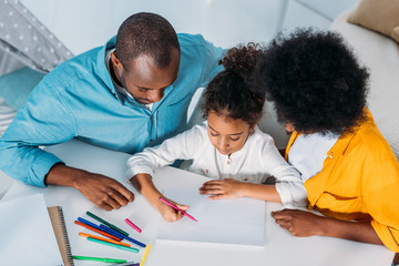 Naklejka premium high angle view of african american parents looking at daughter paint at home