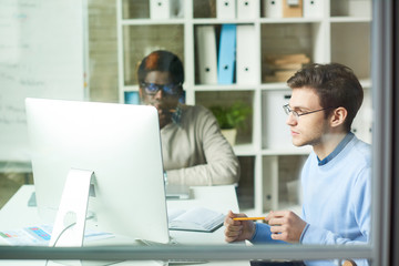 Portrait of two young web developers, one of them African,  working on  IT project while using computers in office, copy space