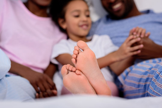 african american parents and daughter lying on bed with feet on foreground