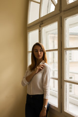 Fototapeta na wymiar Beautiful brunette model in white shirt standing at the window at the morning