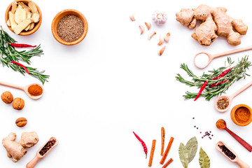 Colorful dry spices in bowls and spoons near ginger, garlic, rosemary, laurel leaf on white background top view copy space