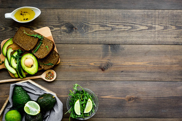 Breakfast for safety weight loss. Avocado toast with rye bread, lime, olive oil and greens on dark wooden background top view space for text