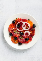 typical Spanish-style salad of red orange, onion and olives with capers and fresh raw olive oil and lime juice . Served on a stone white table. summer healthy snack or light lunch