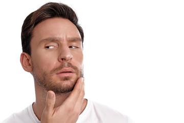 Obraz premium Handsome bearded man cares about his clean healthy skin is isolated on a white background. Guy touches his face with concerned thoughts
