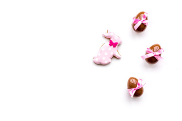 Sweets for Easter table. Chocolate eggs near cookies in shape of Easter bunny on white background top view copy space