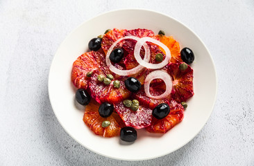 typical Spanish-style salad of red orange, onion and olives with capers and fresh raw olive oil and lime juice . Served on a stone white table. summer healthy snack or light lunch