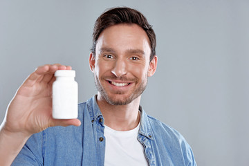 Handsome bearded man isolated on a white background with a bottle of pills. He trusts this medicine...