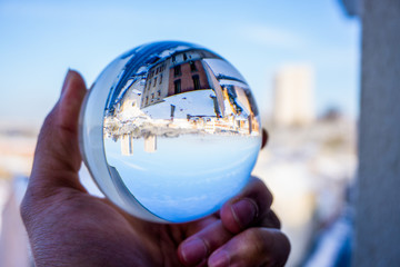 A hand holding a crystal ball for optical illusion. City as the background. Known as an orbuculum,...