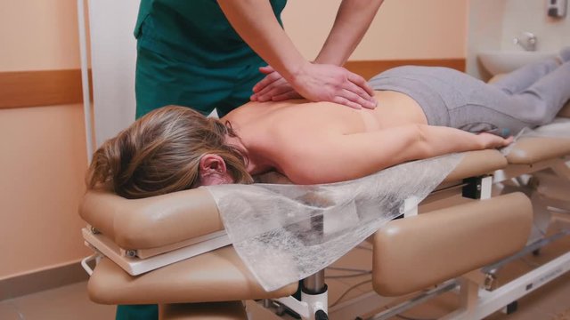 Manual therapist massaging a woman lying on a massage table, pushing on the back strongly