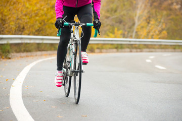 Fototapeta na wymiar Young Woman in Pink Jacket Riding Road Bicycle on the Highway in the Cold Autumn Day. Healthy Lifestyle.