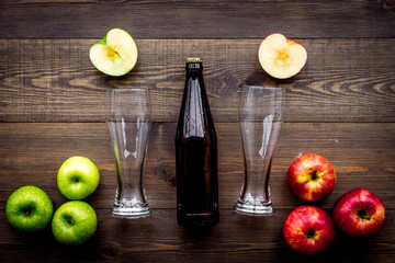 Apple cider. Low-alcoholic beveradge in dark bottle near beer glasses and fresh apples on dark wooden background top view copy space
