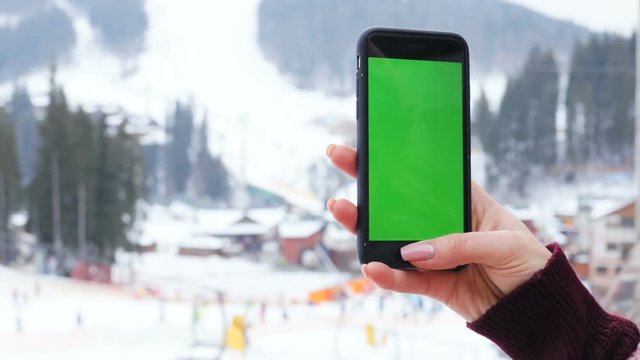 closeup view female woman hand holding modern smart phone mobile blurred background people skis ski winter mountains vacation green screen chroma key mockup application map app video call chat 3G