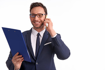 Handsome bearded businessman in office suit and tie isolated on white background. Professional bank manager is holding a blank clipboard while talking on a phone