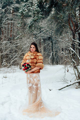 Fototapeta na wymiar Beautiful bride in a fur coat in a winter pine forest with a wedding bouquet