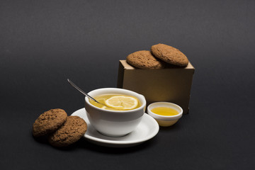 Cookies in carton box near tea on dark grey background.