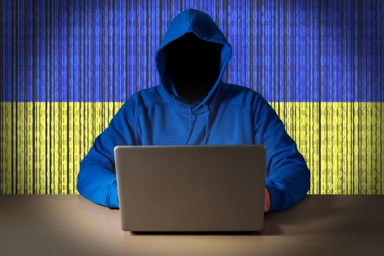 Hacker sitting in front of a laptop on background of digital flag of Ukraine. Cyber Security concept.