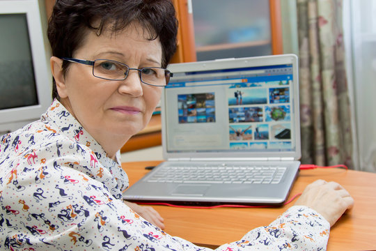 Positive senior woman sitting at the notebook at home and looking pictures on travel sites