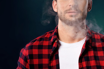 Handsome bearded man smoking electronic vape cigarette, Guy in a red t shirt smoking vapor, Man exhaled vapor on a dark studio background. Man smoking e-cigarette