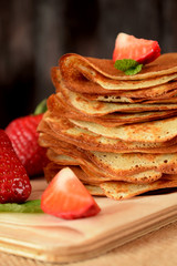 Golden crepes piled on a wooden board surrounded by fresh strawberries