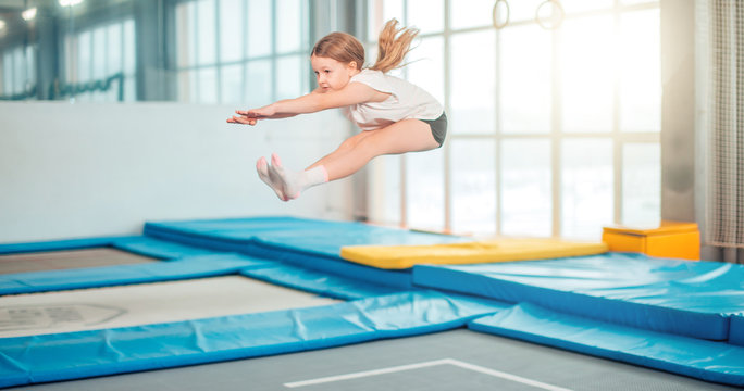 Girl jumping high in striped tights on big trampoline.