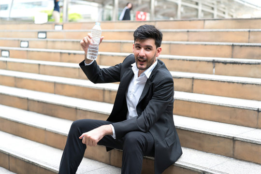 Happy businessman showing water bottle at stairs outdoors.