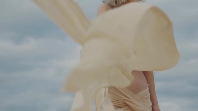 Divine woman is posing half naked on a cloudy weather on the beach. She is dressed in silk cloth and holding silk stripes in her hands.