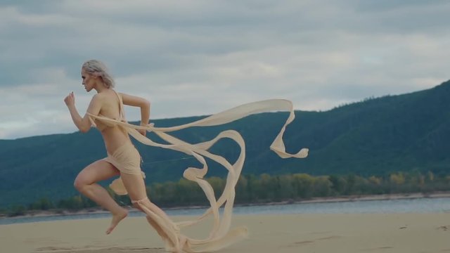 a fantastic desert character quickly runs along the sand to the sea, the woman's clothes flutter in the wind, the lady jumps up and confidently heads towards the water