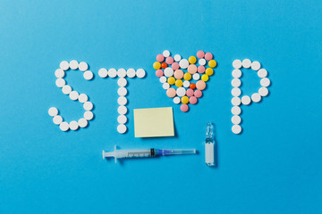 Medication white, colorful round tablets in word Stop isolated on blue background. Pills heart ampoule syringe needle, empty paper sticker sheet. Concept of health treatment choice, healthy lifestyle.