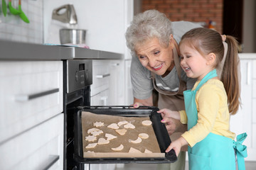 Cute little girl and her grandmother making cookies on kitchen